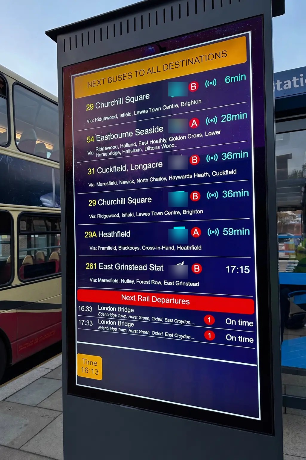 Outdoor freestanding passenger information totem in use beside public transport vehicles